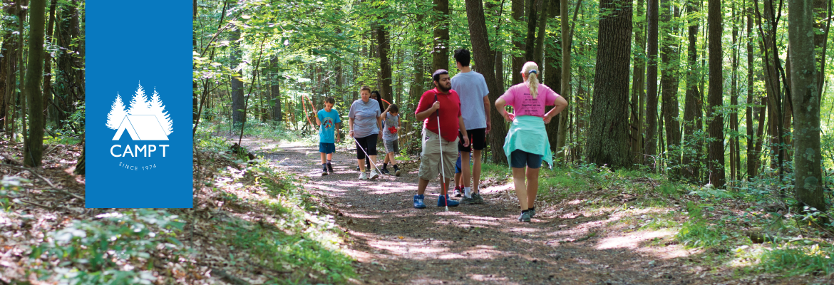 A group of visually impaired hikers use canes to navigate a wooded trail