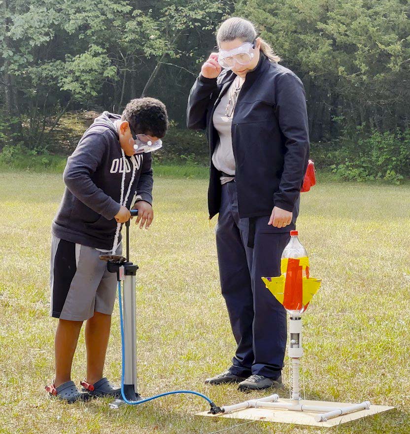 Camp director Jill Teegardin assists a student as he pumps air into his bottle rocket in the middle of a large field.