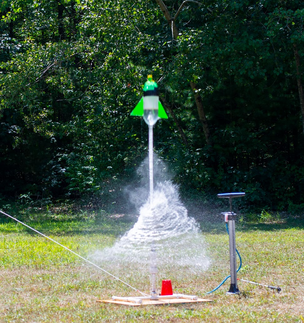 A soda bottle rocket shoots into the air, shooting water downward in a spiral.