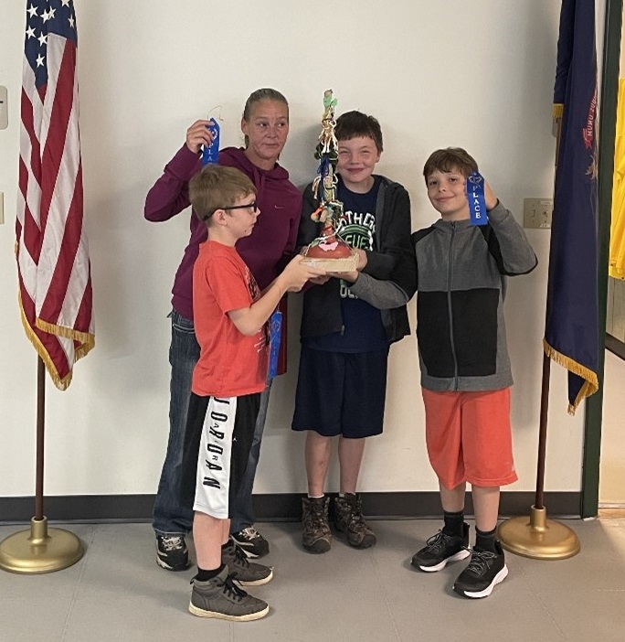 A mother and her three sons pose for a photo with a trophy and three blue ribbons.