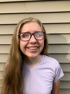 Sarah smiles for a portrait photo outside next to a house.