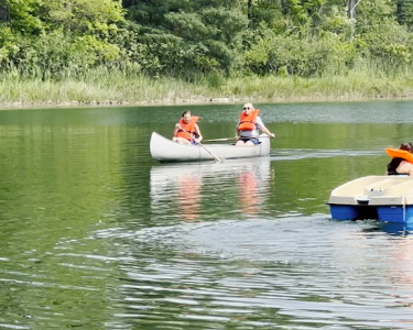 Two campers in a canoe and two campers in a paddle boat on Flannigan Lake at Camp T.