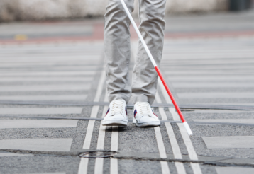 A person crossing a street and using a white cane.