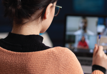 A woman with dark hair and glasses on a zoom meeting call. She is holding a pen