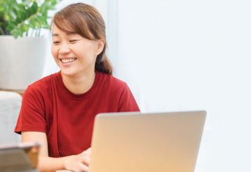A mother and daughter smile while sitting at a table with a laptop and tablet.