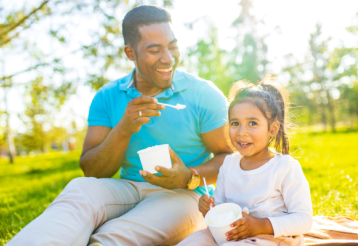 A man eating ice cream with his daughter in a park. 