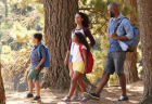 A man, woman, and two children smile as they walk through a forest on a sunny day.
