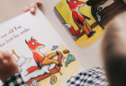 View from above of a young child reading an illustrated storybook about a fox who has lost his socks.