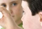 View from behind a young boy who is wearing a hearing device. Another young boy in front of him signs the letter