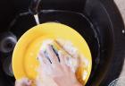 Closeup of a child's hands washing a yellow plate with a sponge over a black sink basin.
