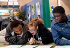 Three students, two boys and one girl, complete a worksheet together while lounging on a carpeted floor at a Finance Park facility.