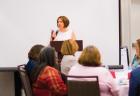 A woman with short brown hair talks into a microphone at a podium in front of a white screen at the 2018 MAER Conference.