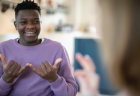 A teenager smiles while talking to someone in American Sign Language.