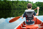 A young boy maneuvers a canoe on a tranquil lake, embraced by stunning scenery.