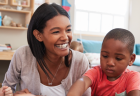 A teacher smiles while sitting with a group of young children in a classroom.