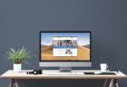 A large computer monitor on a desk, showing the MDE-LIO website. The desk features a plant, headphones, keyboard, and mug.