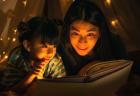 A woman and young daughter smile while reading a book in a tent at night, surrounded by twinkle lights.