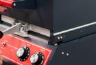 Closeup of a woman's hands pressing the top of a thermoform machine toward the base. A small red instrument panel on the front features a switch and knobs for time and heat.