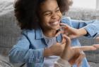 A child smiles while communicating in sign language with an adult.