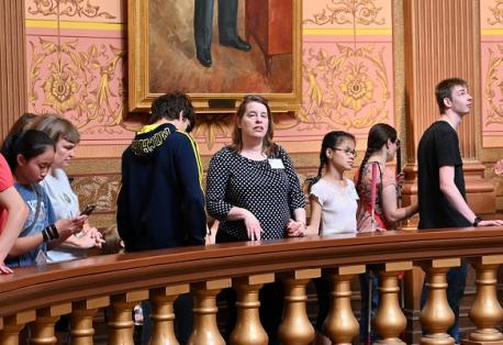 Several adults and children stand next to a large circular railing as a tour guide describes features of the Lansing capitol building.