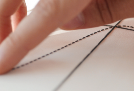 Closeup of fingers touching a raised tactile graph on white paper.