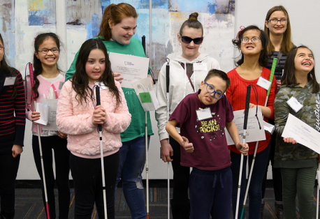 Twelve students, ranging from elementary to high school age, smile for a group photo. Most of the students are holding white canes.