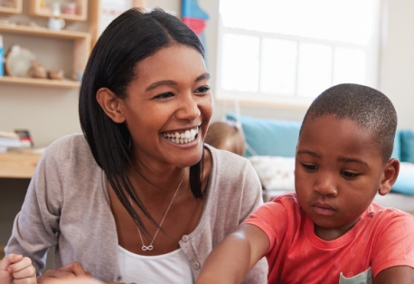 A teacher smiles while talking to young children in a classroom.