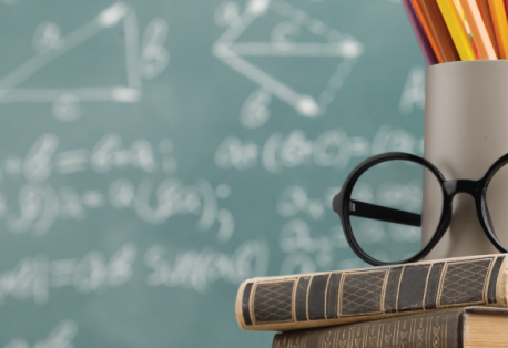 A mug and glasses rest on top of two books in front of a chalkboard.