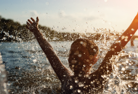 A child raises his hands in the air while playing in a lake on a sunny day.