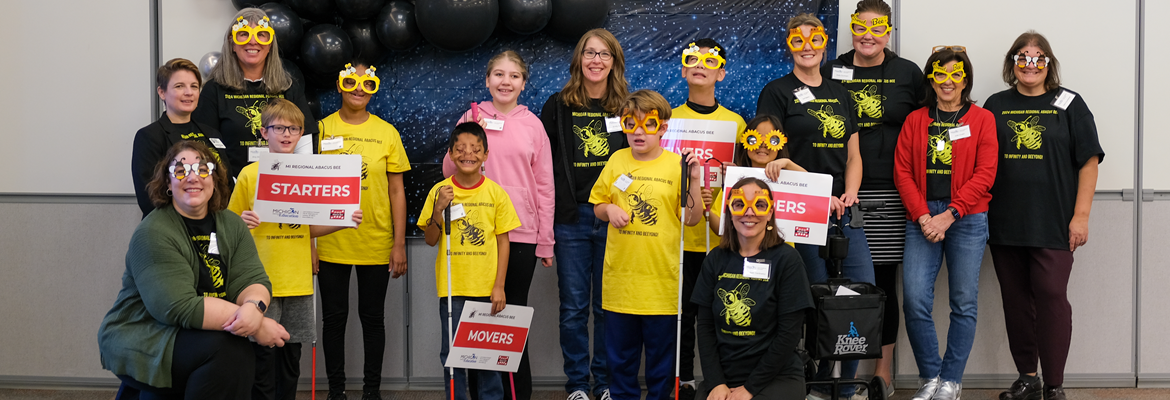 A group of contestants and volunteers at the Michigan Abacus Bee against a starry sky backdrop and black balloons.