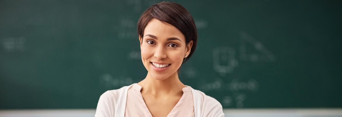 A woman smiles at the camera while standing in front of a chalkboard.