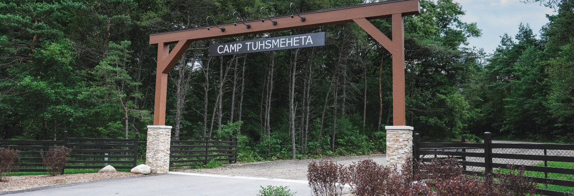 The entrance arch at Camp Tuhsmeheta, featuring wooden beams and the camp's name.