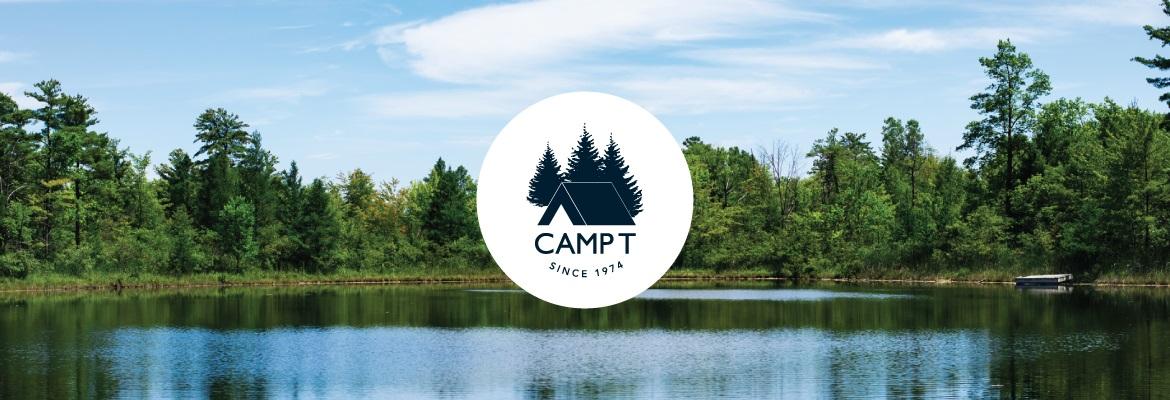 The lake at Camp T surrounded by pine trees on a sunny day. The Camp T logo is on the image.