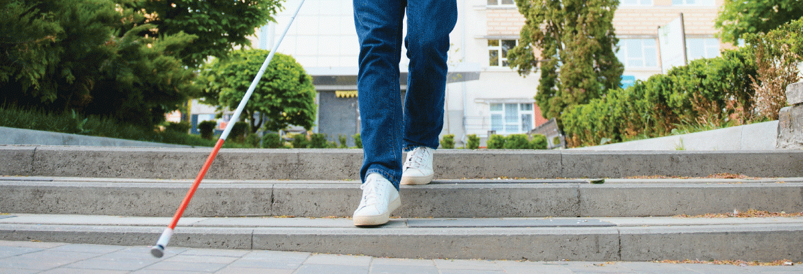 Closeup of someone's jeans and shoes as they walk down three steps outside with a white cane.