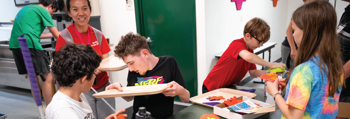A group of student sit around a table doing a craft activity at Camp T. 