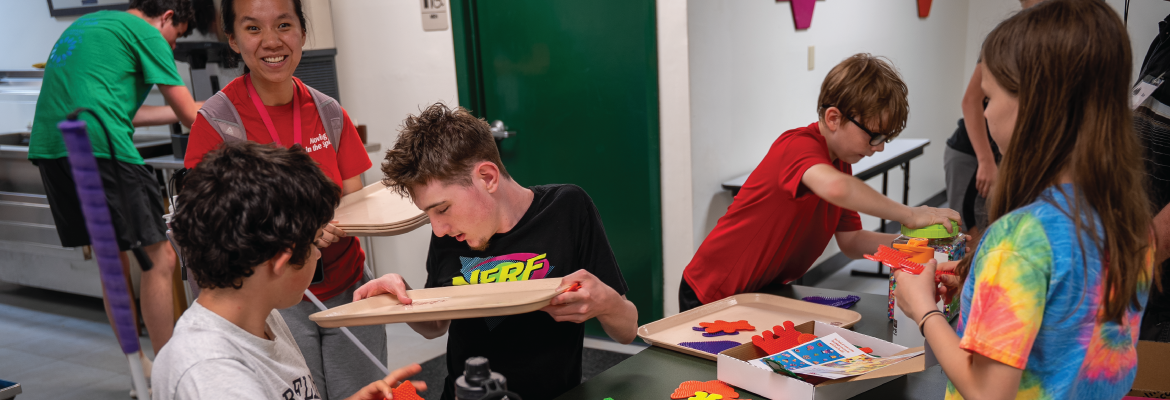 A group of student sit around a table doing a craft activity at Camp T.