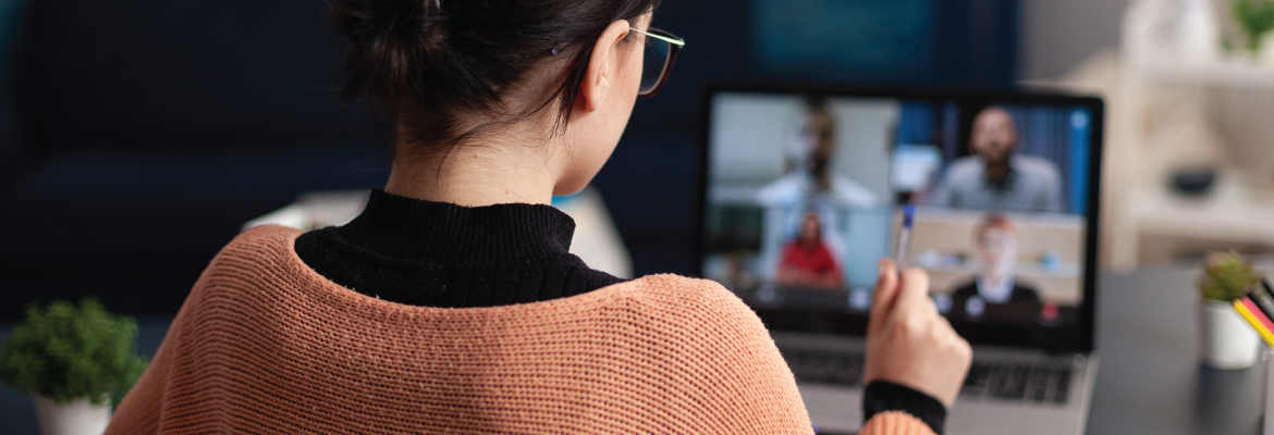 A woman with dark hair and glasses on a zoom meeting call. She is holding a pen 