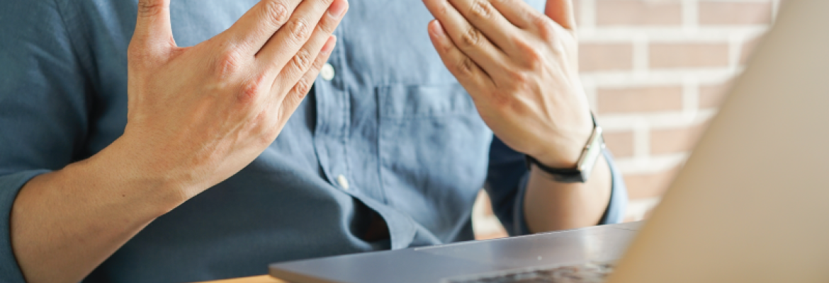 A man sits in front of a laptop at home and uses his hands to communicate.