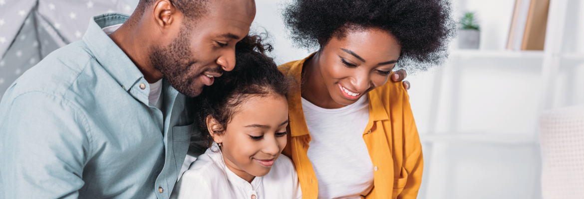 A mother, father, and young girl smile as they read a book together.