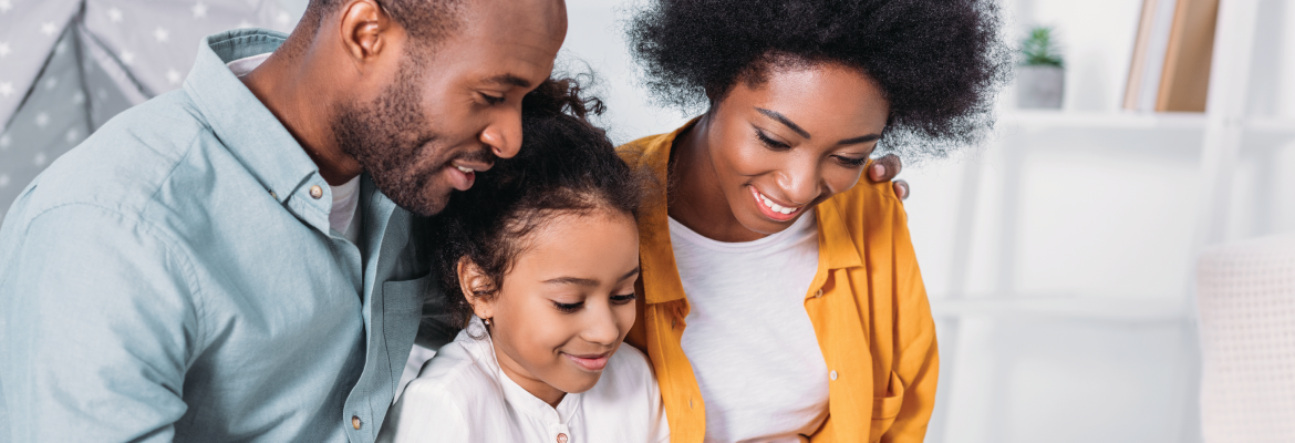 A mother, father, and child smile while reading together at home.