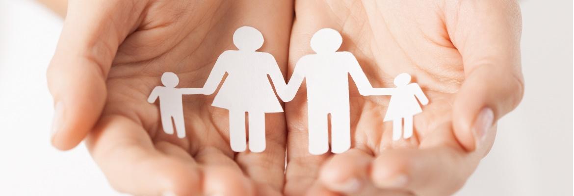 Closeup of a person's hands holding a paper stick figure cutout of a male figure and female figure holding hands with two smaller child figures.