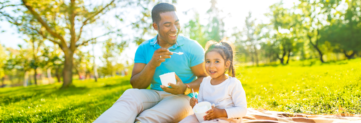 A man eating ice cream with his daughter in a park. 
