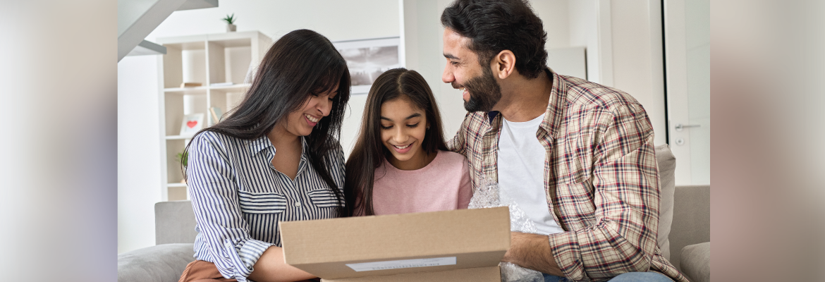 A family smiles as they open a brown shipping box.