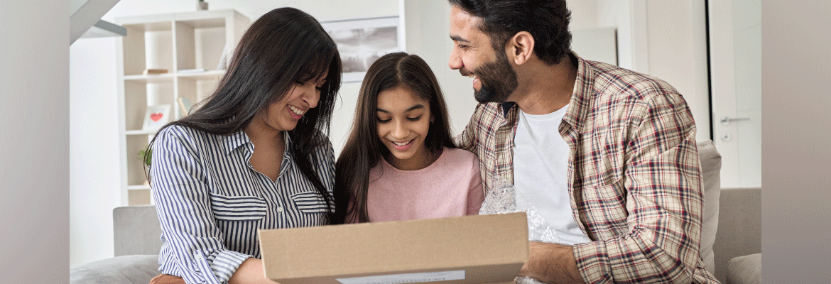 A family smiles while opening a brown shipping box. 