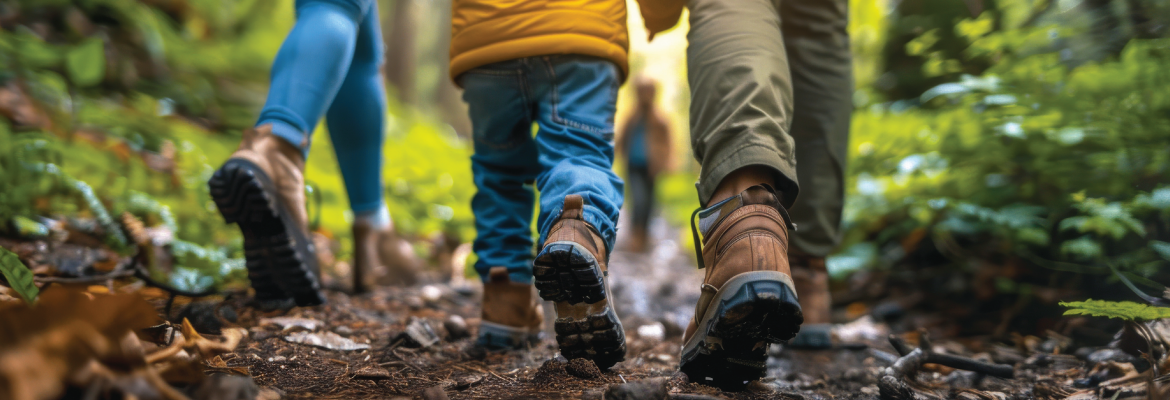 A close-up of feet walking on a forest trail, highlighting a child and two adults in colorful outdoor attire, surrounded by lush greenery.