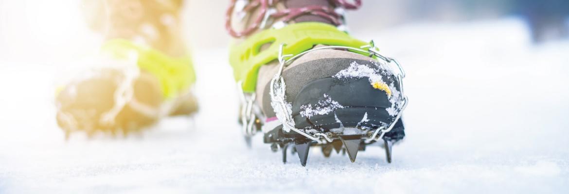 Closeup of a person's boots with ice cleats in the snow.