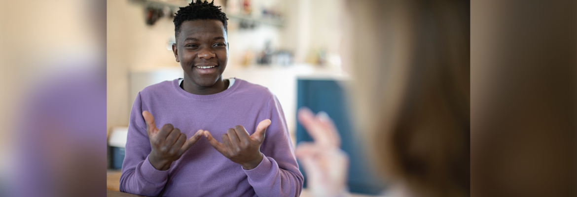 A teenager smiles while talking to someone in American Sign Language.