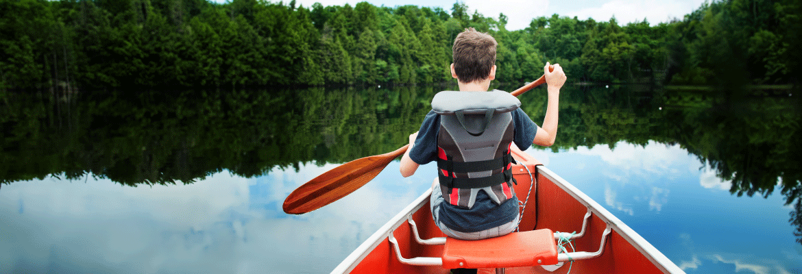 A young boy maneuvers a canoe on a tranquil lake, embraced by stunning scenery.