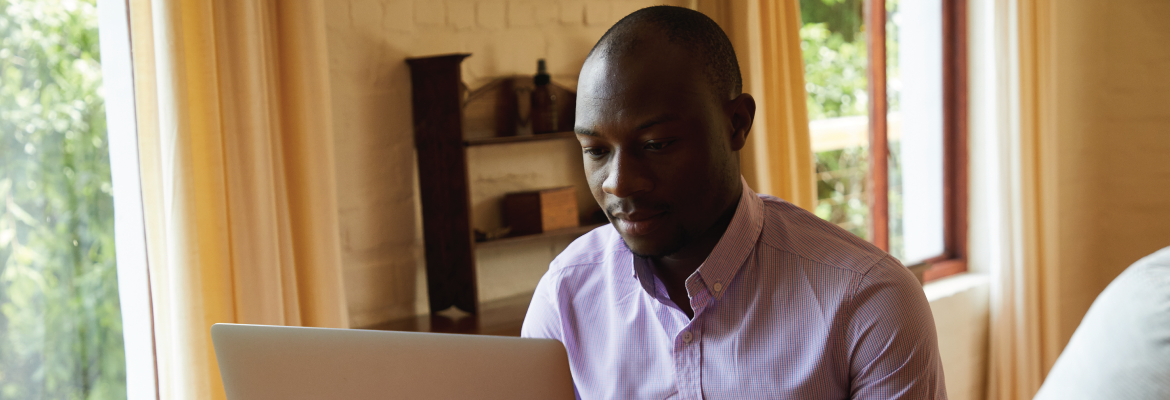 A man wearing a button-down shirt looks at an open laptop on the table in front of him.