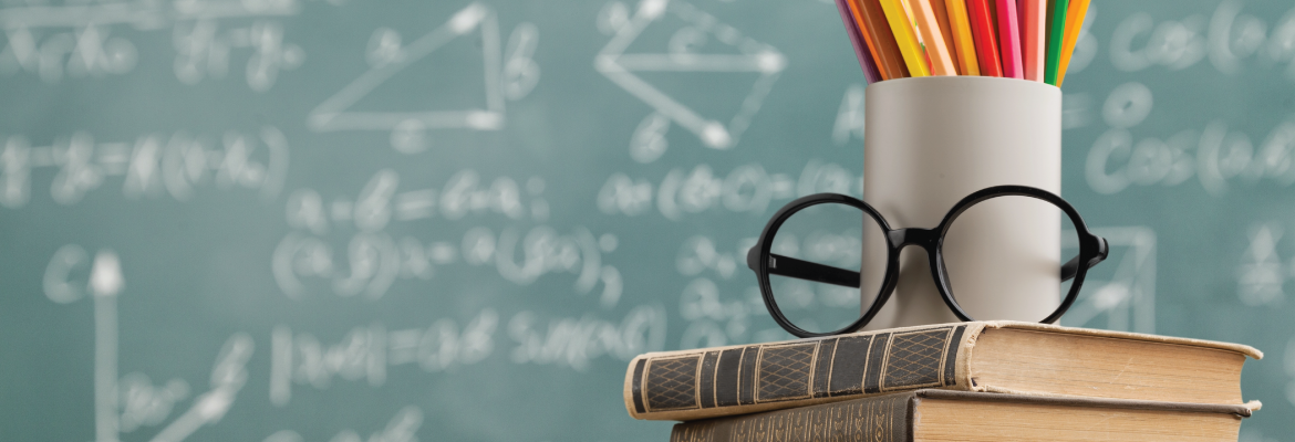 A mug and glasses rest on top of two books in front of a chalkboard.